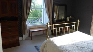Um quarto com cama, cômoda, janela com cortinas e escrivaninha com espelho.