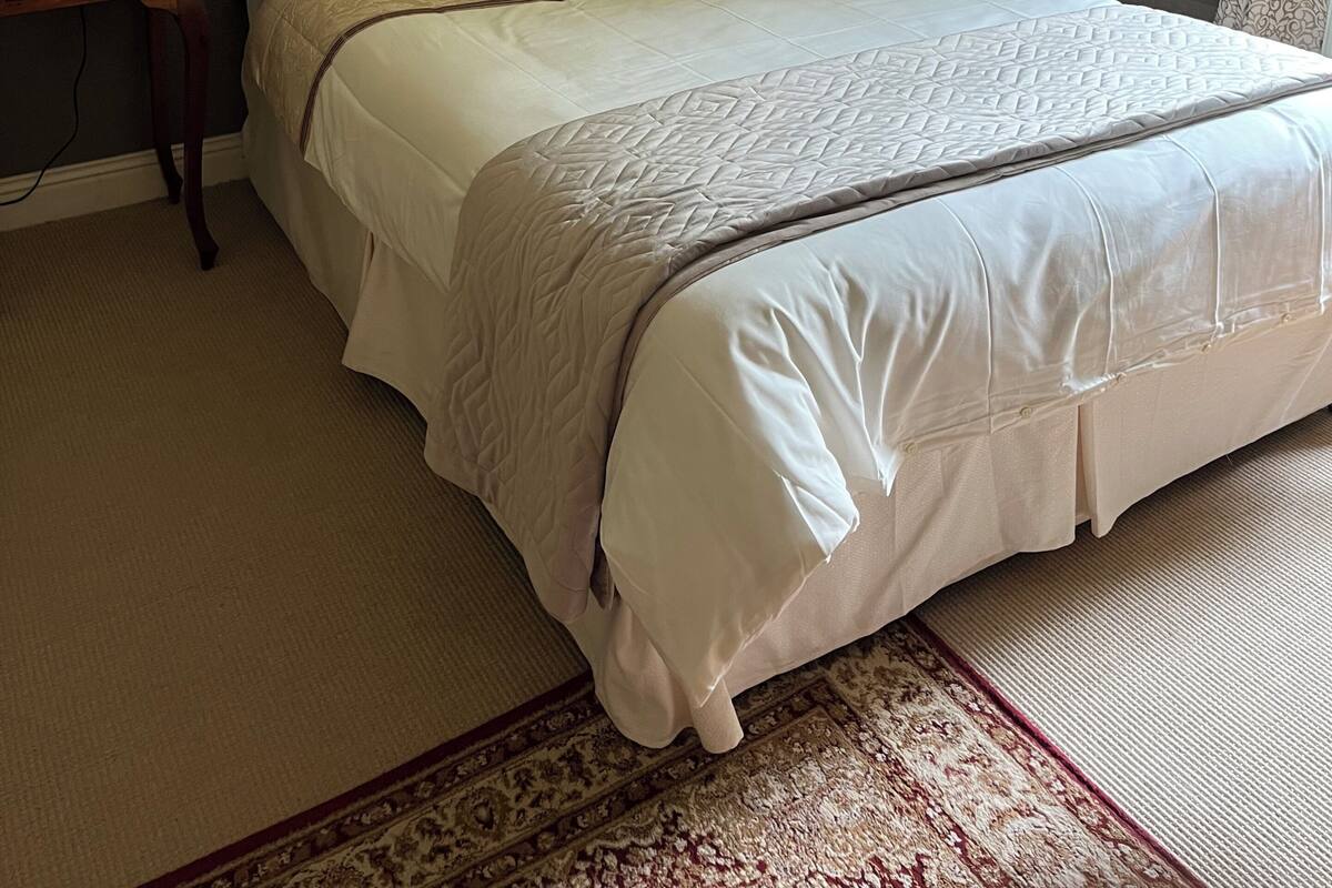 A neatly made bed with a patterned bedspread, two bedside tables with lamps, a framed picture on the wall, and a patterned rug on the floor.