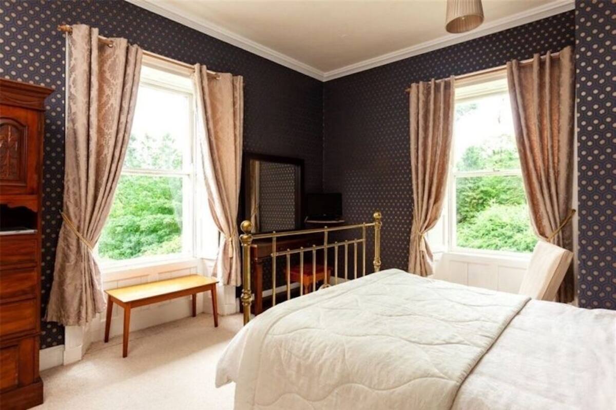 A bedroom with a bed, a wooden bench, a television, and a window with curtains.