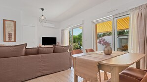 A modern living room with a sofa, TV, dining table, and large windows. - Bed & Breakfast «Pomme reinette» – Shared Pool, Wi-Fi & Air Conditioning (Le Val)