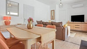 A modern living room with a sofa, TV, and a dining table with chairs. - Bed & Breakfast «Pomme reinette» – Shared Pool, Wi-Fi & Air Conditioning (Le Val)