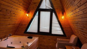 Eine Holzhütte mit einem dreieckigen Fenster, einer Badewanne und zwei Stühlen.