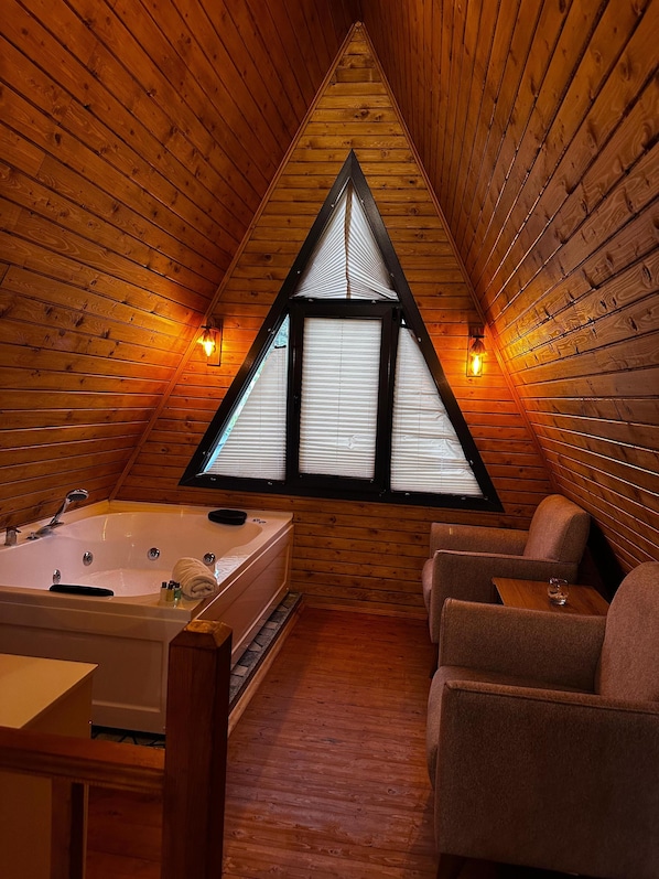A wooden cabin with a triangular window, a bathtub, and two chairs.