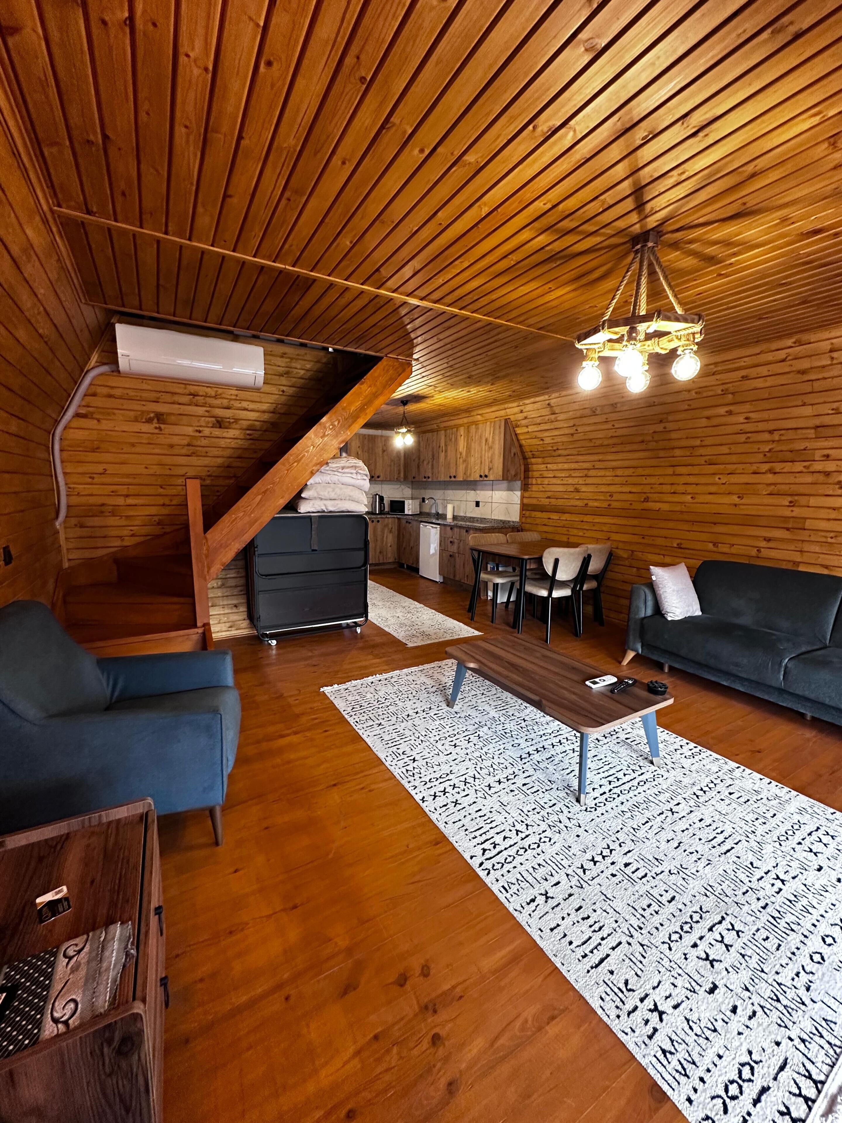 A wooden interior with a staircase, a kitchen, a sofa, and a coffee table.