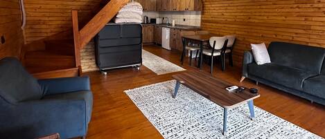 A wooden interior with a staircase, a kitchen, a sofa, and a coffee table.