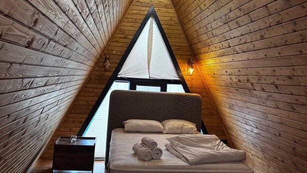 Ein dreieckiger Raum aus Holz mit einem Bett, einem Nachttisch und einem Fenster an der Spitze.