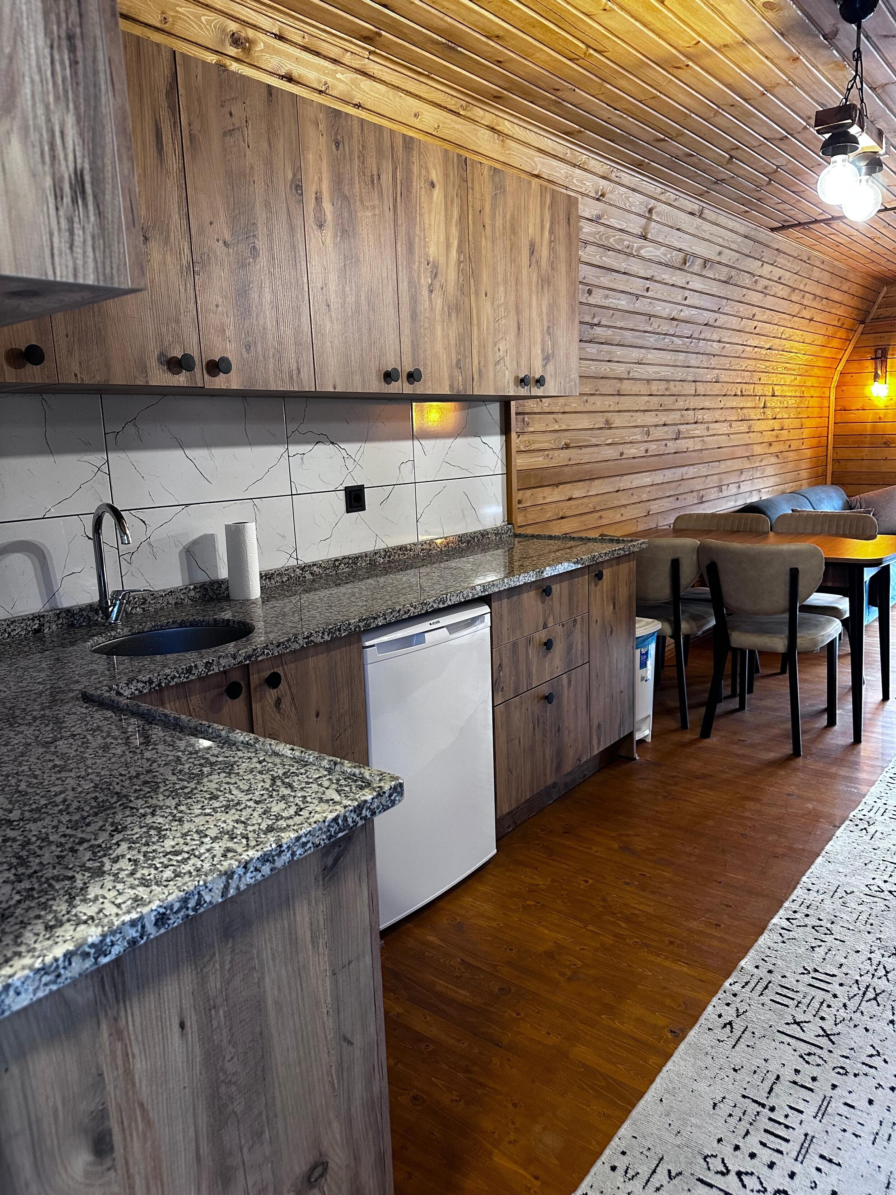 A kitchen with wooden cabinets, a granite countertop, a dishwasher, and a dining area with chairs and a table.