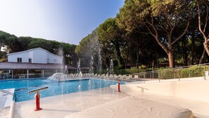 A swimming pool with water jets, a white building, and trees in the background. - Jesolo Family Resort (Jesolo)
