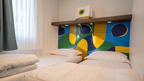 A hotel room with two beds, a colorful abstract wall art, a shelf with a bag, and a window with curtains. - Jesolo Family Resort (Jesolo)