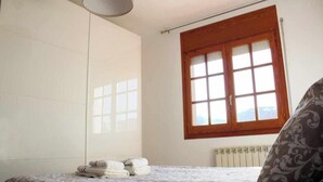 Een slaapkamer met een bed, een raam met uitzicht, een radiator en een stapel handdoeken.