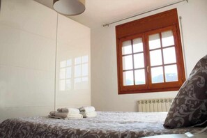 A bedroom with a bed, a window with a view, a radiator, and a towel stack. - VACATIONS IN MARESME HOUSE FOR 7 PEOPLE (El Masnou)
