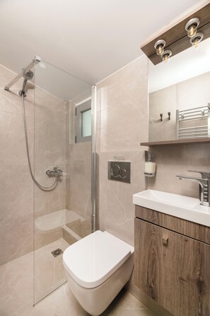 Ein modernes Badezimmer mit einer Duschkabine, einer Toilette und einem Waschtisch mit Spiegel und Handtuchhalter.