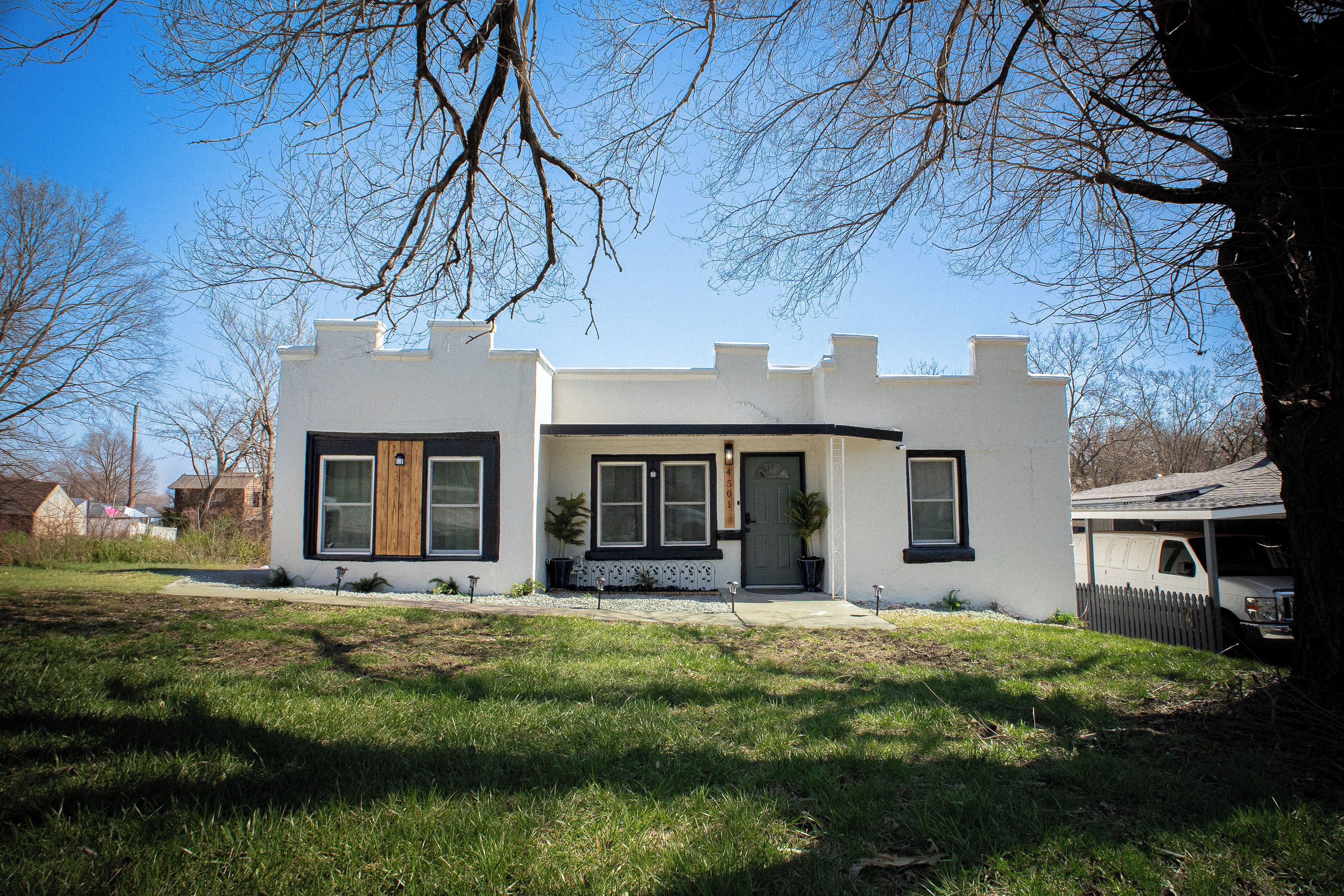 Une maison moderne à deux étages, avec une façade blanche, des éléments décoratifs noirs et un porche à l’avant.