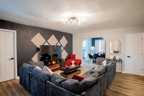 A modern living room with a sectional sofa, a fireplace, and a dining area in the background.