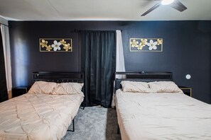A room with two beds, a ceiling fan, and dark walls.