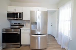 A kitchen with stainless steel appliances, white cabinetry, and a wooden floor.