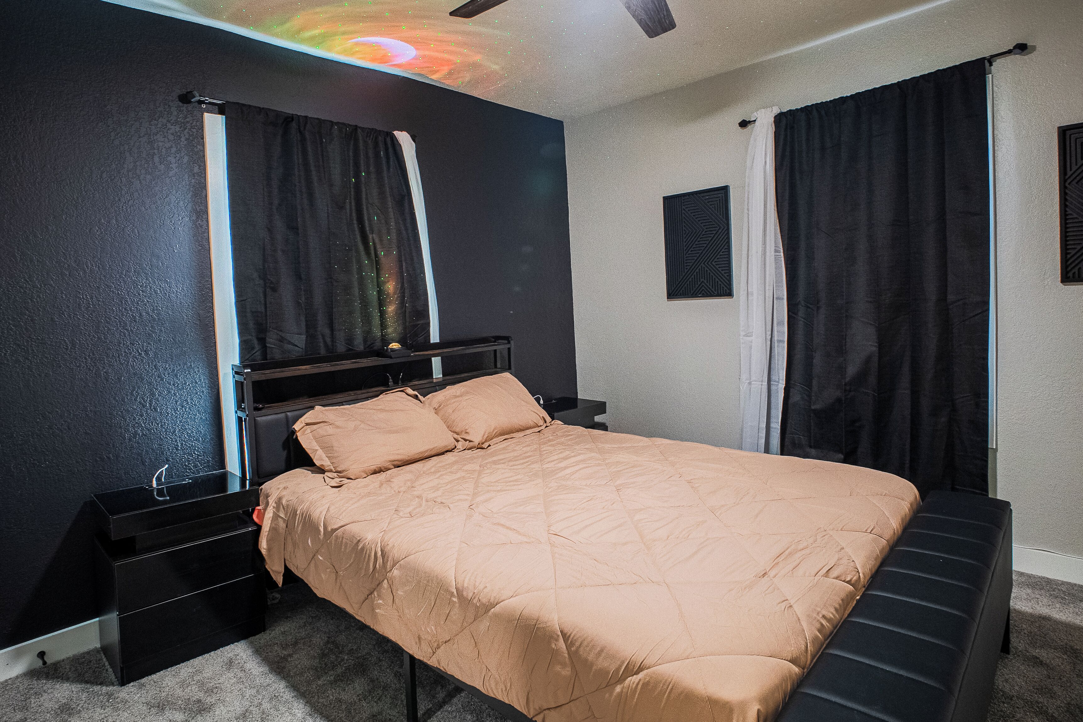 Ein Schlafzimmer mit Bett, Nachttischen, Kommode, Deckenventilator und Projektionsschirm.