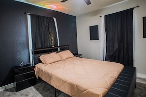 A bedroom with a bed, nightstands, a dresser, a ceiling fan, and a projector screen.