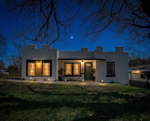 A modern two-story house with a well-lit entrance, large windows, and a visible address number.