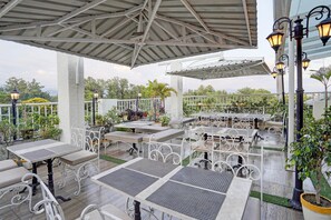 An outdoor patio area with white metal tables and benches, surrounded by potted plants and a white fence. - Deluxe Room Gold Stone Comfort (Dehradun)