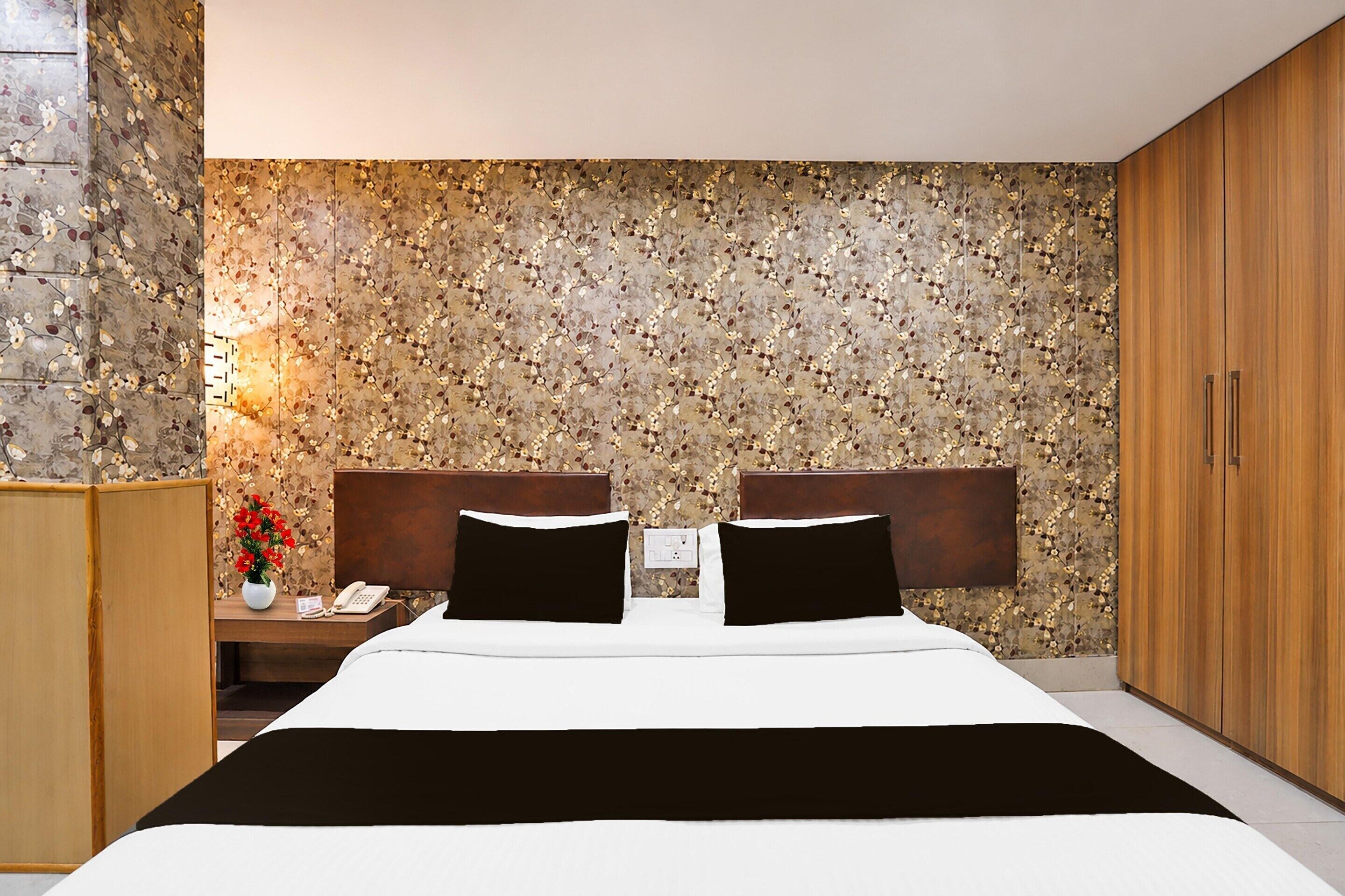 A hotel room with a bed, a nightstand, a telephone, a vase with flowers, and a wardrobe.