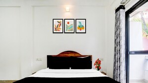 Een bed met houten hoofdbord, wit beddengoed en een zwart accent. Boven het bed hangen drie kunstwerken in lijstjes.