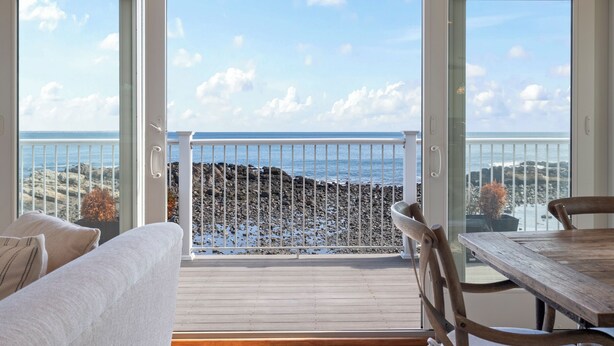 A balcony with a view of the sea, a wooden table, and a sofa.