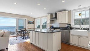 A modern kitchen with a central island, white cabinetry, stainless steel appliances, and a view to the outside.
