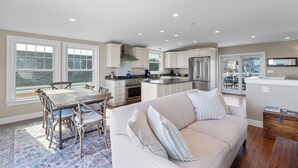 A modern kitchen with white cabinets, a central island, and a dining area with a wooden table and chairs.