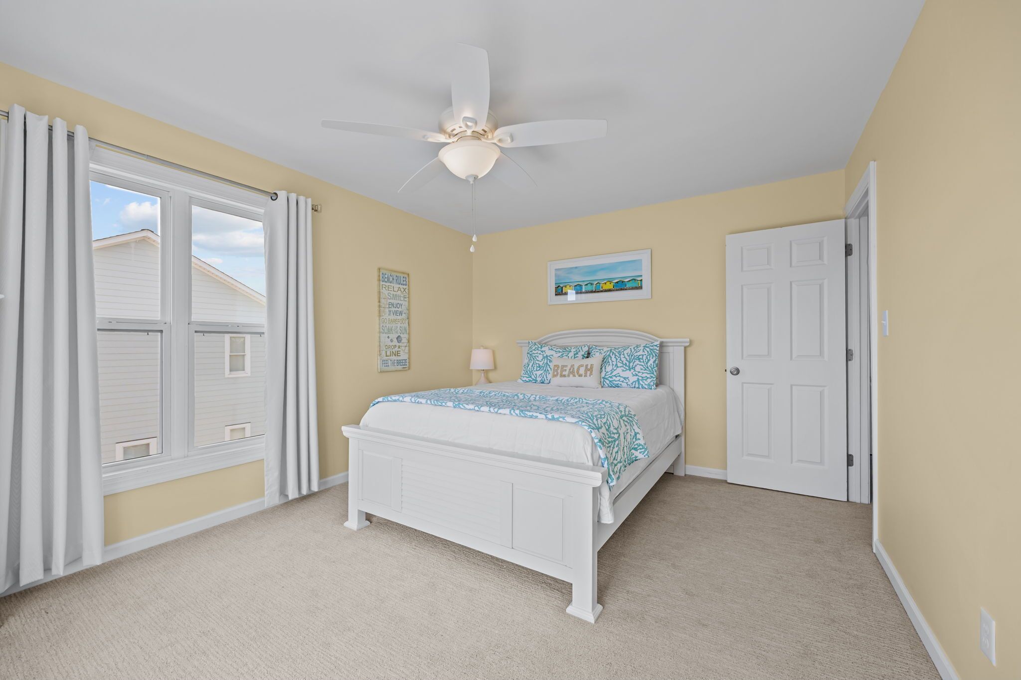 Quarto com cama, ventilador de teto, porta e janela com cortinas.