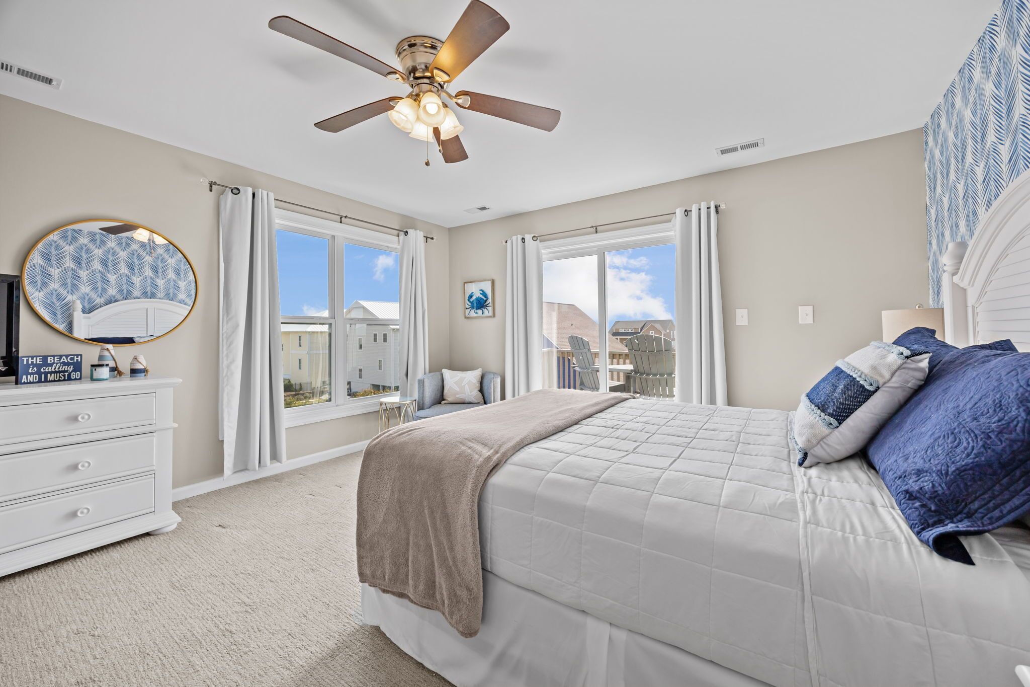 A bedroom with a bed, ceiling fan, dresser, and large windows.