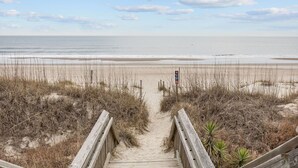 Een houten looppad dat naar een strand leidt, onder een heldere lucht.