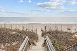 Ein hölzerner Steg führt zu einem Strand unter blauem Himmel.