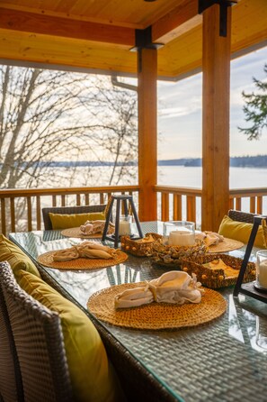 Ein Tisch mit Glasplatte, gewebten Untersetzern, gelben Kissen und Blick auf einen See.