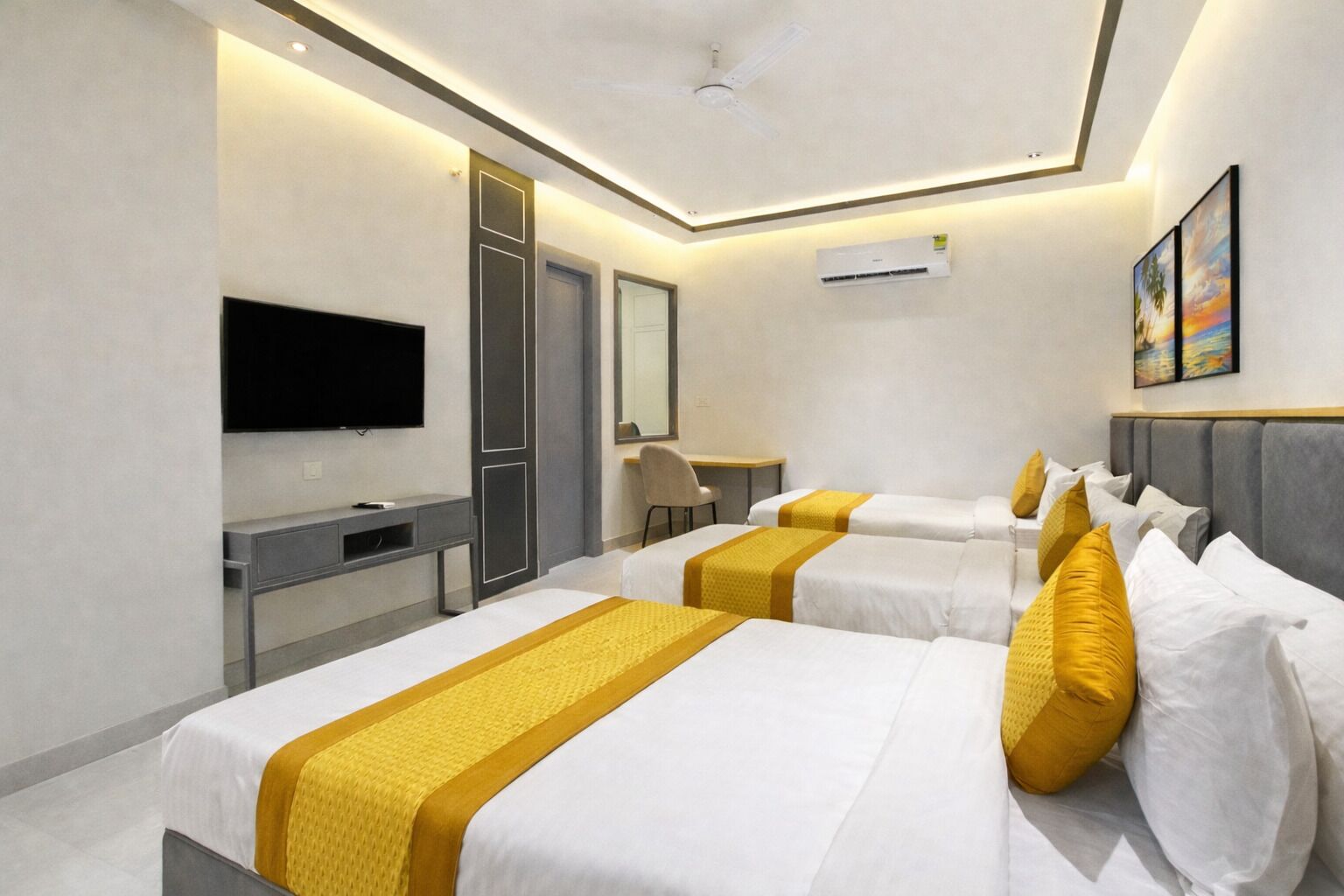 A hotel room with two beds, a desk, a TV, and an air conditioning unit.