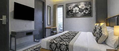 A modern bedroom with a large bed, a flat-screen TV, a desk, and a painting on the wall.