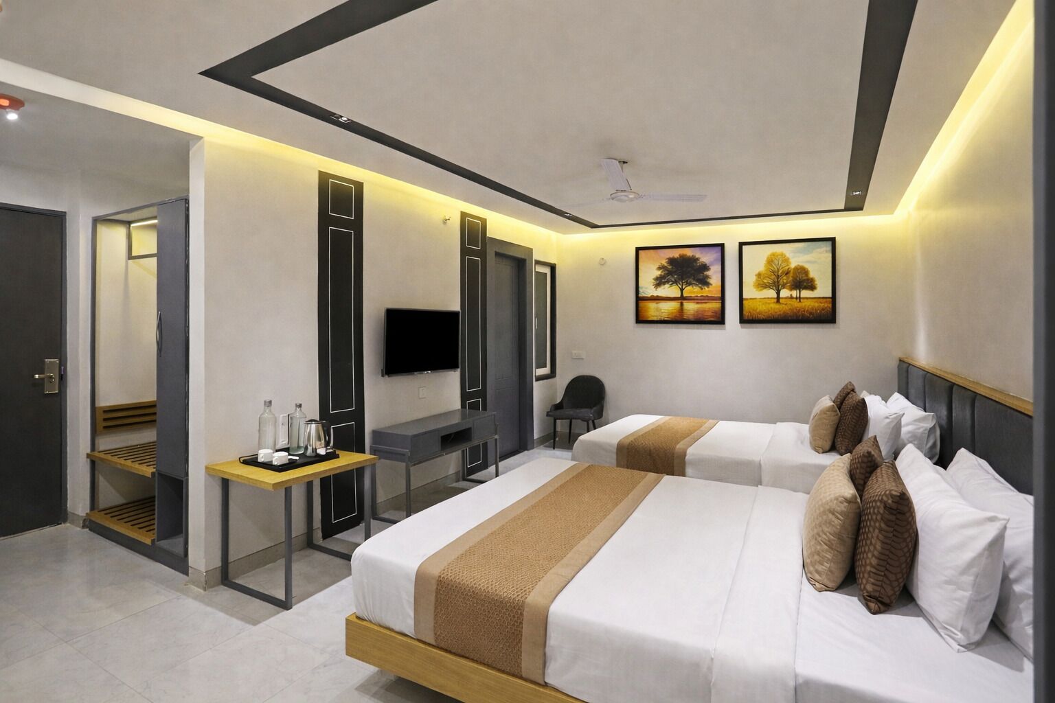 A modern hotel room with two beds, a desk, a TV, and artwork on the wall.