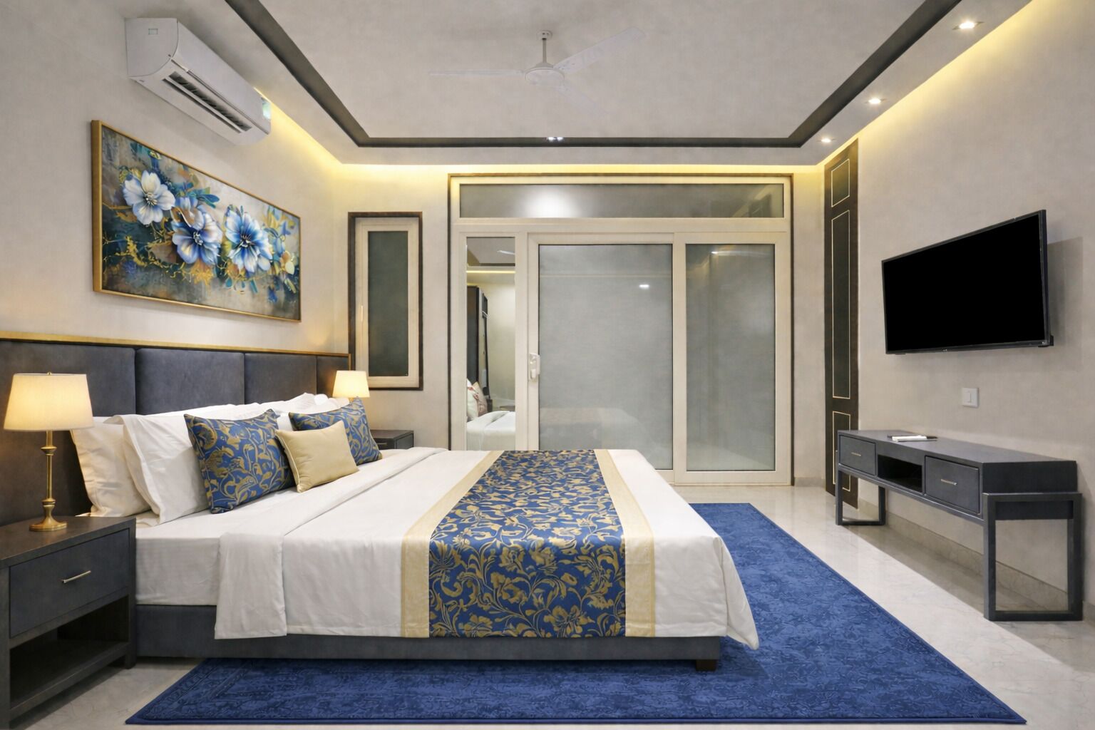 A modern bedroom with a large bed, bedside tables, a flat-screen TV, and a sliding glass door leading to a bathroom.