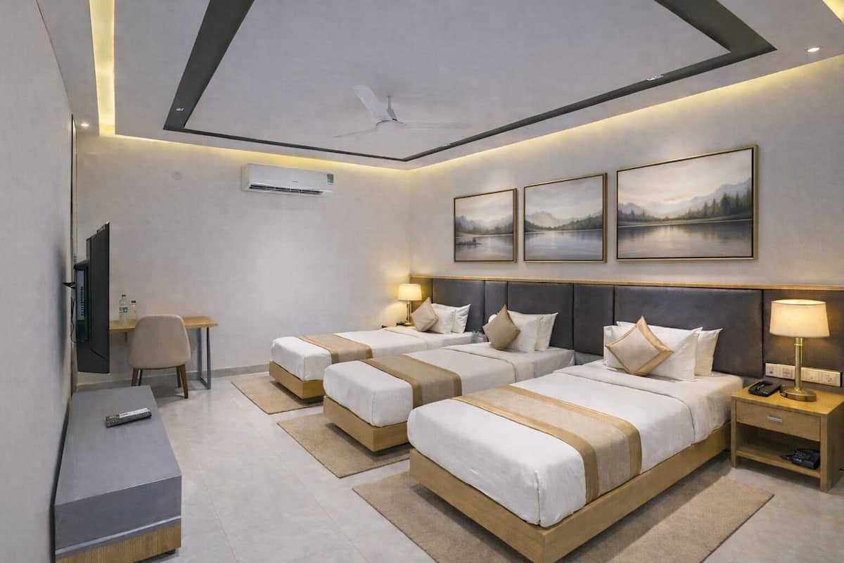 Ein Hotelzimmer mit zwei Betten, einem Schreibtisch, einem Sessel, einem Fernseher und Bildern an der Wand.