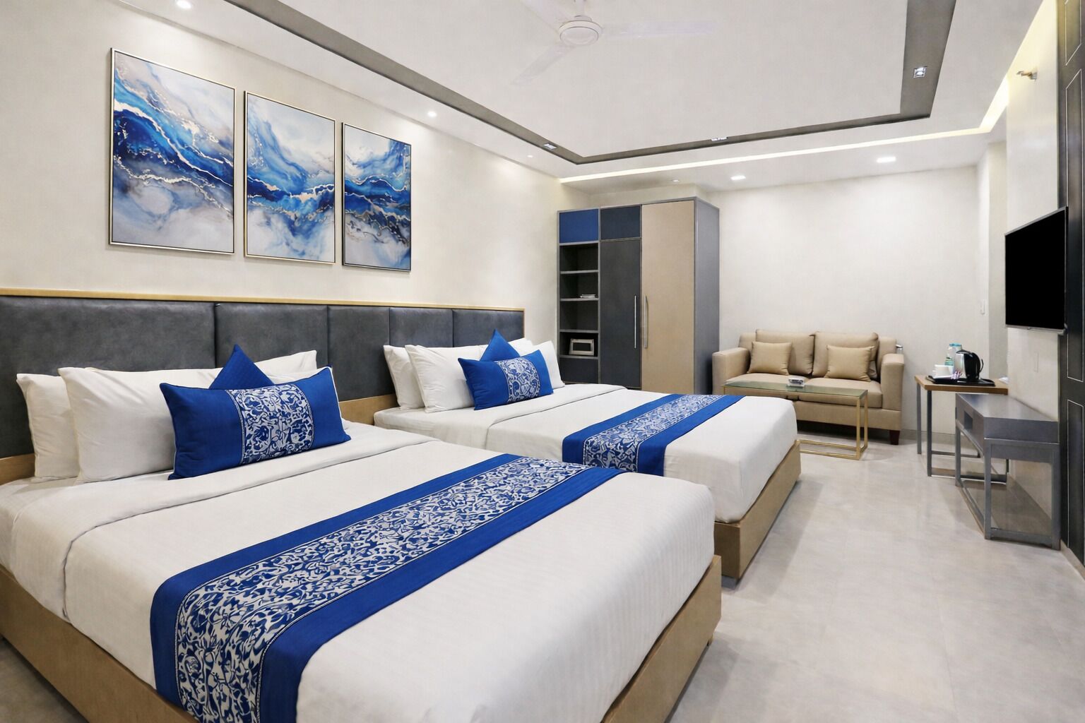 A hotel room with two beds, a sofa, a TV, and artwork on the wall.