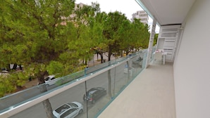 A balcony with a glass railing overlooking a street with cars and trees. - Perfect Holiday Flat Close to the Beach (Lignano Sabbiadoro)