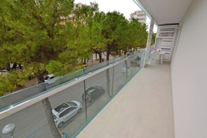A balcony with a glass railing overlooking a street with cars and trees. - Perfect Holiday Flat Close to the Beach (Lignano Sabbiadoro)