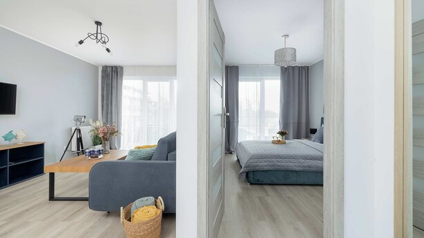 A modern room with a sofa, a small table, a tripod, and a bed. - Stylish Apartment | Balcony, Parking, Wellness Area (Dziwnów)