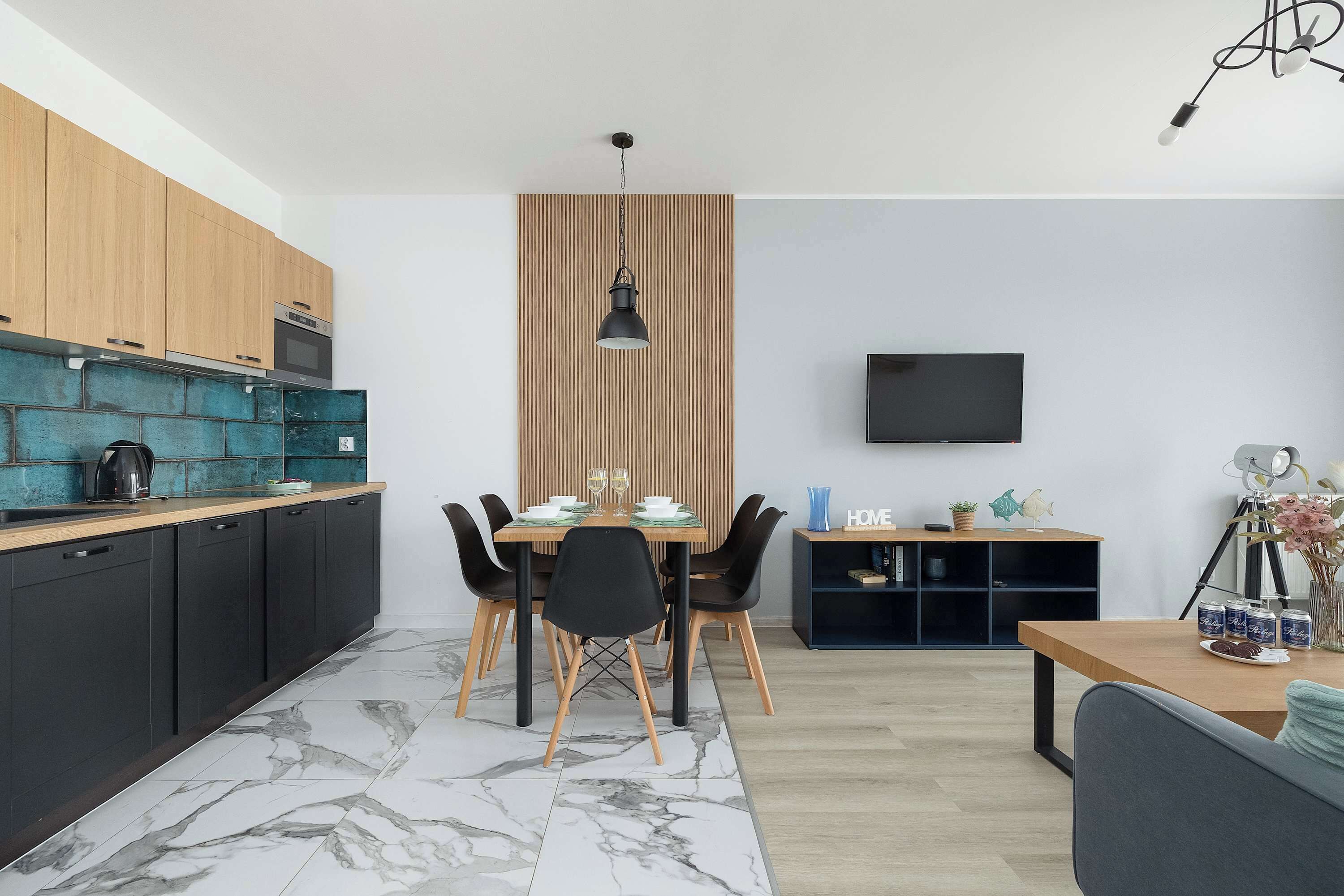 Een moderne keuken met een eethoek, een aan de muur bevestigde televisie en een houten kast.