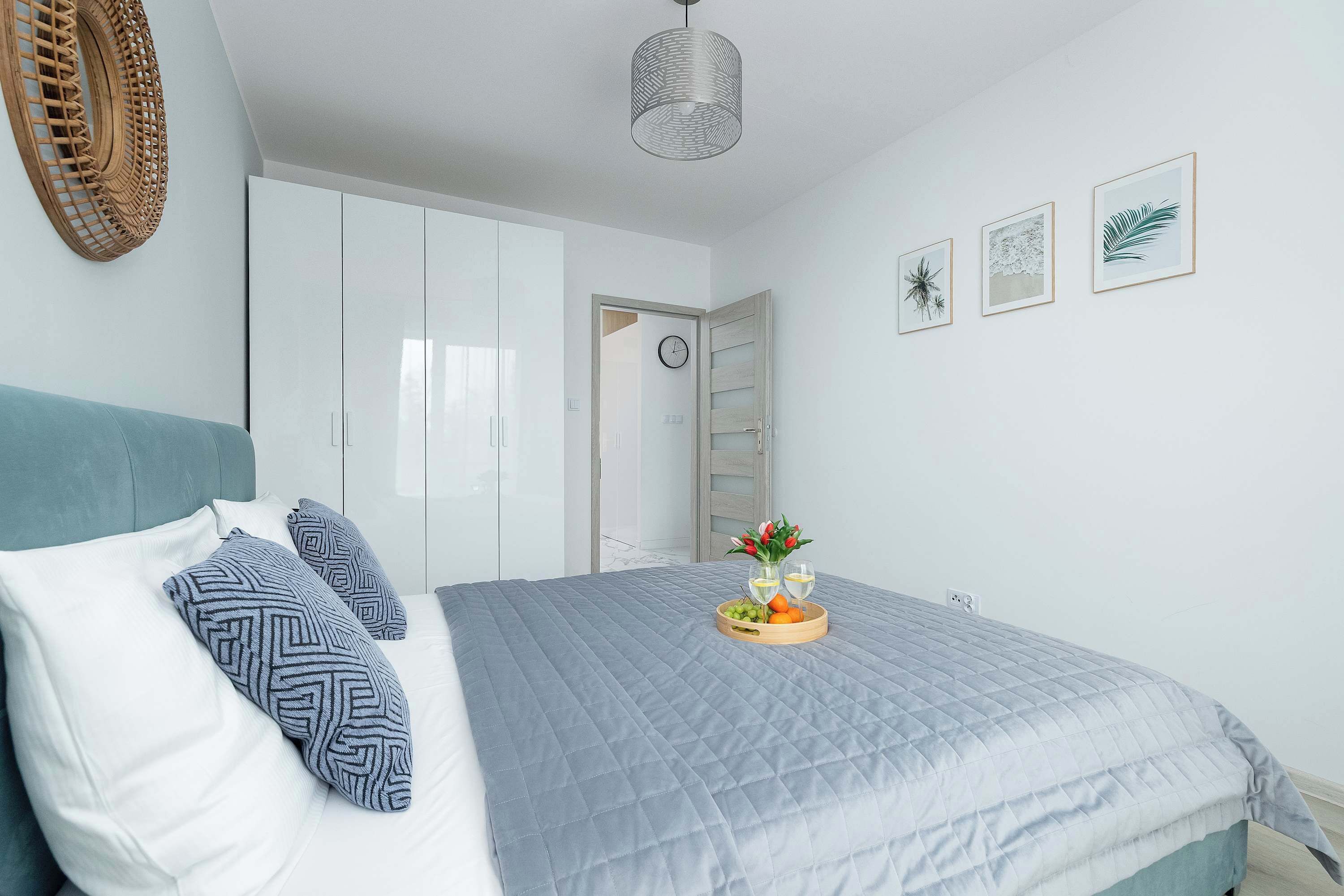 Ein Schlafzimmer mit einem Bett, Kissen, einem Nachttisch mit Obstplatte und Gläsern, einem Kleiderschrank und Wandbildern.
