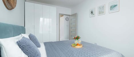 Ein Schlafzimmer mit einem Bett, Kissen, einem Nachttisch mit Obstplatte und Gläsern, einem Kleiderschrank und Wandbildern.