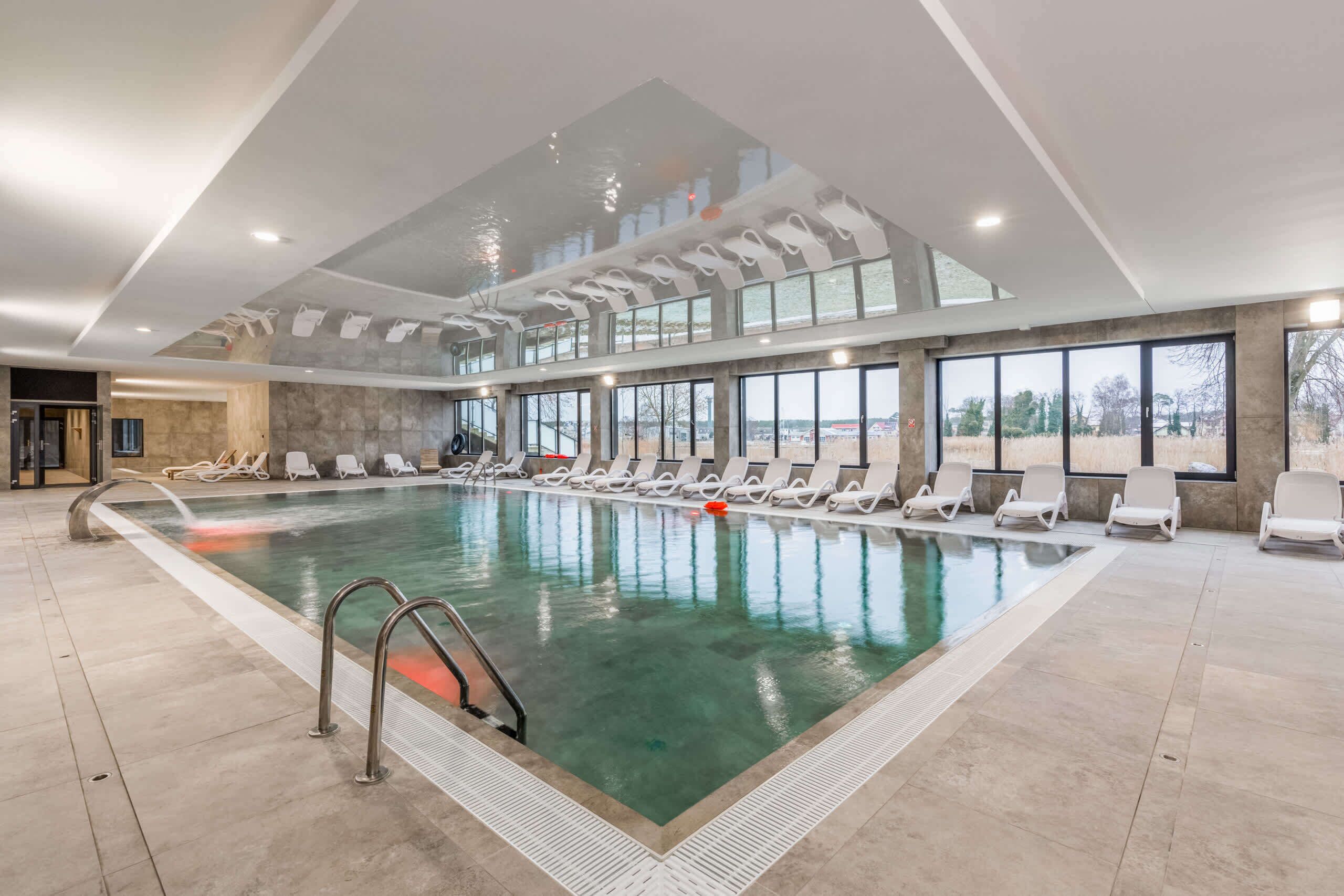 A large indoor swimming pool with clear water, surrounded by lounge chairs and a modern ceiling design.