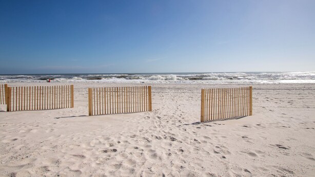 Ein Strand mit einer Holzlattenzaun und Fußabdrücken im Sand.
