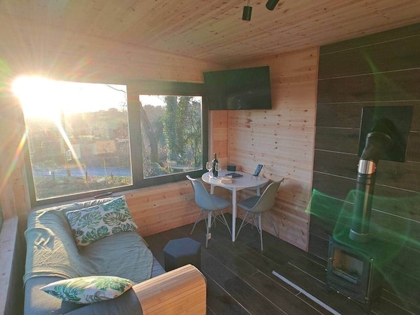 Un acogedor interior de cabaña con sofá, mesa de comedor, sillas, chimenea y un amplio ventanal con vistas.