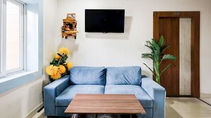 A room with a blue sofa, a wooden coffee table, a TV mounted on the wall, a wooden door, and a potted plant. - Deluxe With Twin Bed Hotelmbansal Residency (Bhubaneshwar)
